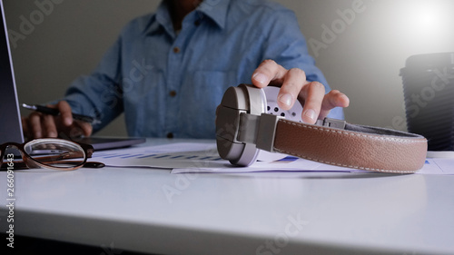 A young blue shirt is picking up brown headphones while working on a laptop.