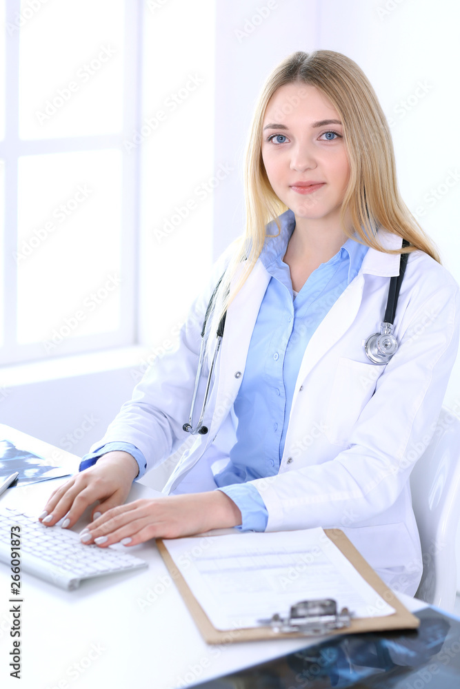 Young woman doctor at work in hospital office. Blue color blouse of therapist looks good. Medicine and healthcare concept