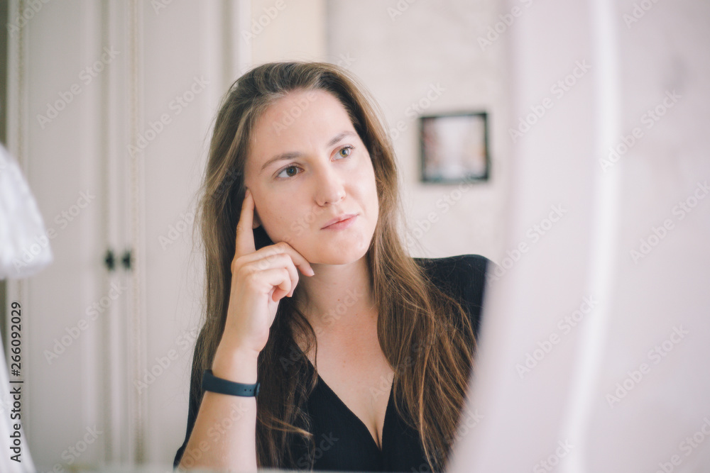 Close-up girl of European appearance thoughtfully sits in front of a mirror in a bright hotel room Close-up girl of European appearance thoughtfully sits in front of a mirror in a bright hotel room