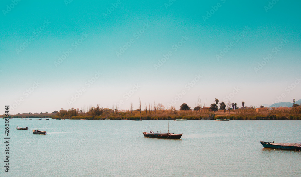 Calm lake with two fishing boats. Fresh water lagoon in Estany de cullera near albufera de Valencia, Spain. Suitable for World Water Day. Teal and orange style