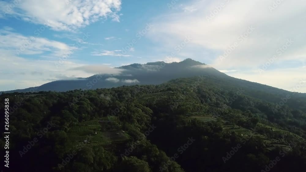 Aerial of green tropical rainforest and Bratan volcanic complex on blue sky background in Bali, Indonesia. Dolly forward shot. Aerial of green tropical rainforest and Bratan volcanic complex on blue sky background in Bali, Indonesia. Dolly forward shot.