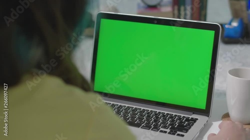 Woman working on the laptop computer with green screen at home. Chroma key. View from the back. 