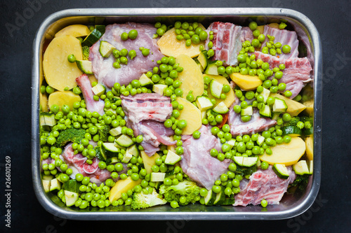 Baking tray full of goat meat with potatoes, broссolis, peas