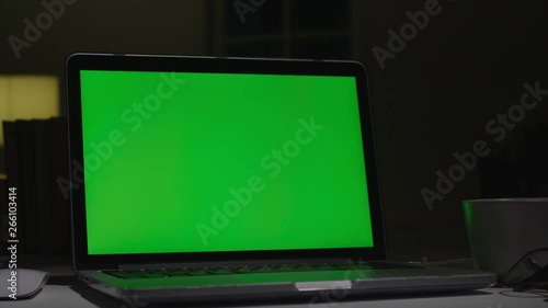 Laptop with green screen. Dark office. Dolly shot. Perfect to put your own image or video.