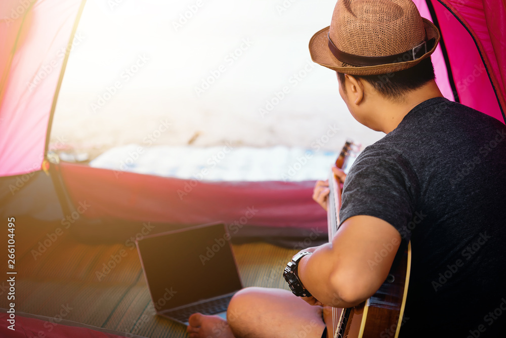 Romantic young man sitting in tent at the beach with playing the guitar.