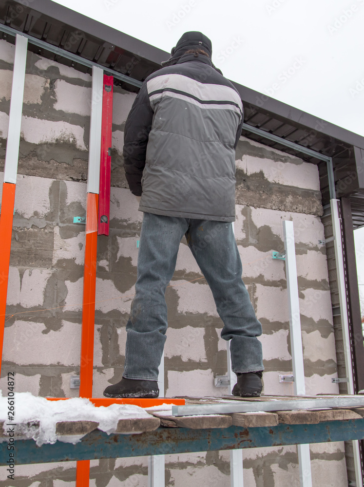 A worker installs a metal profile on the walls of a siding house