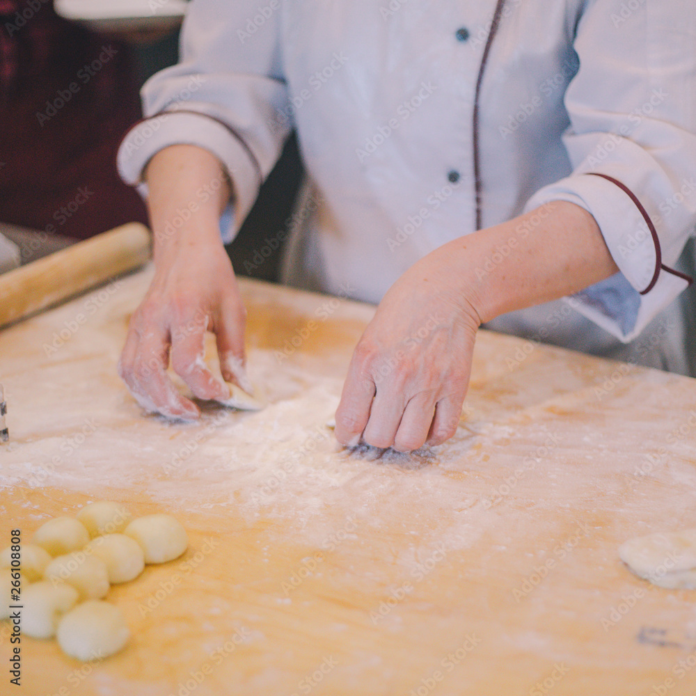 Close-up of female hands in white cook coat knead the dough on the wooden table in the restaurant