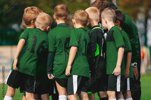 Group of Young Boys in Green Jersey Shirts Standing with Coach on Soccer Field. Sports Team Putting Their Hands in Together. Pre-game Coach Speech. Junior Kids Sports Team with Coach