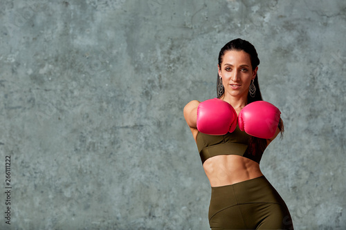 Beautiful athletic girl posing in pink boxing gloves on a gray background. Copy space, close-up. Concept sport, fight, goal achievement. © Georgii