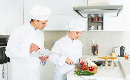 Female and male cooks are making salad on their work place in the kitchen