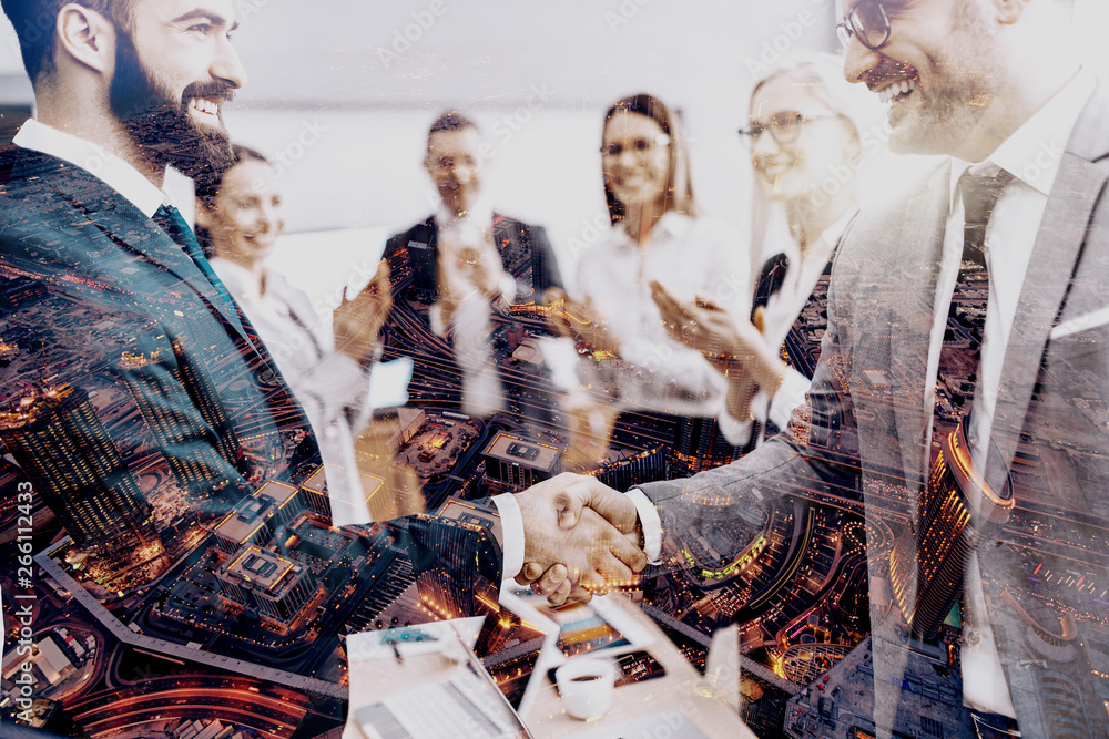 Obraz premium Two successful businessmen shaking hands while other colleagues clapping. Double exposure technique used.