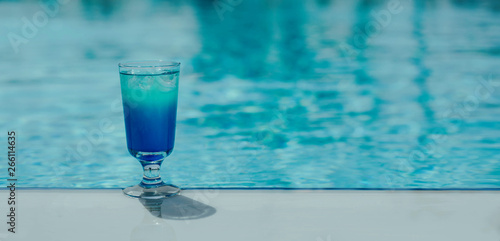 Blue coctail with ice in the glass on the swimming pool background. Resort tropical hotel in summer day and fresh water. Blurred backgraund with copy space  banner size.