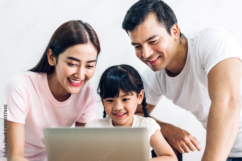 Happy family father and mother with daughter sitting and looking at laptop computer together in the living room at home Happy family father and mother with daughter sitting and looking at laptop computer together in the living room at home
