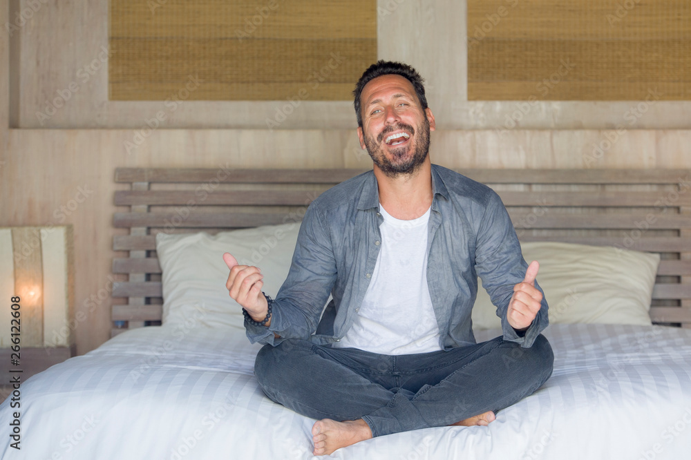 Fototapeta premium interior portrait of 30s to 40s happy and handsome man at home in casual shirt and jeans sitting on bed relaxed at home smiling confident and happy feeling positive