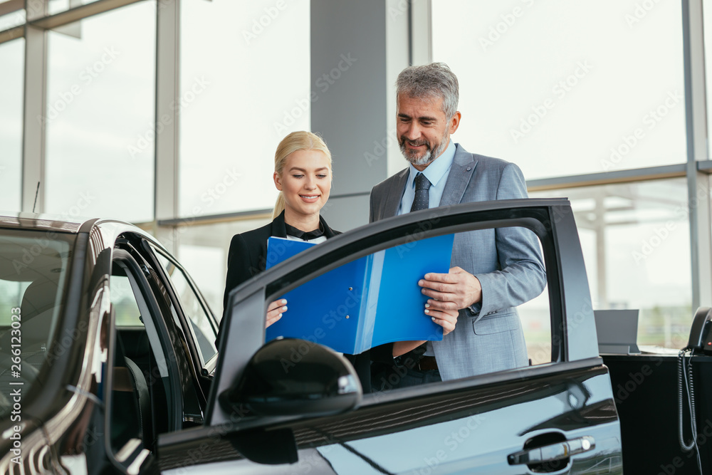 senior sales agent showing car brochure to customer in car dealers showroom senior sales agent showing car brochure to customer in car dealers showroom