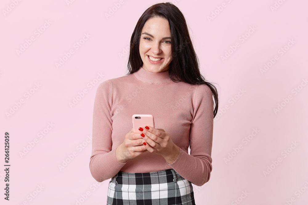 Close up portraite of cute Caucasian woman using smart phone for texting or chatting with her friend, hearing funny news, laughing with joy and happy, isolated over pink background. Copy space. Close up portraite of cute Caucasian woman using smart phone for texting or chatting with her friend, hearing funny news, laughing with joy and happy, isolated over pink background. Copy space.