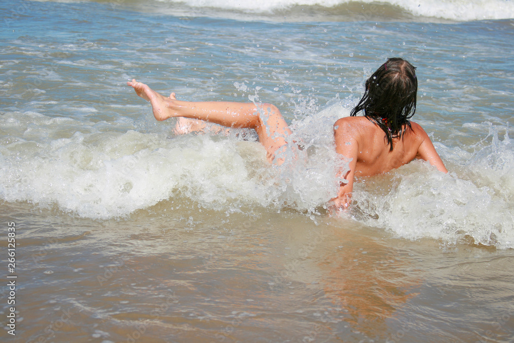 Beautiful photo with a young girl swimming in the sea in rolling waves, around the water spray and sea foam Beautiful photo with a young girl swimming in the sea in rolling waves, around the water spray and sea foam