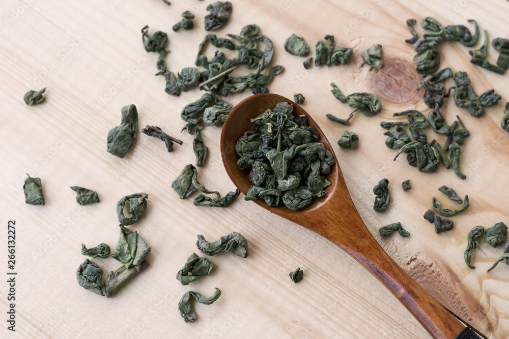 Green tea leaves in a wooden spoon on wooden table
