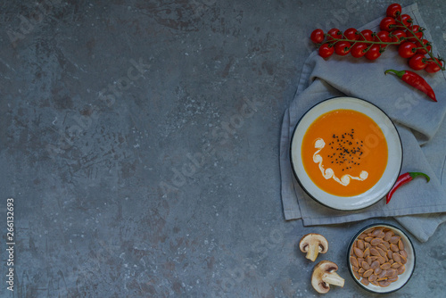 Pumpkin soup in a bowl with autumn vegetables and pumpkin seeds. Vegan soup. Vegetables cream soup and ingredients. Top view. Concept of healthy eating or vegetarian food. Top view with copy space.