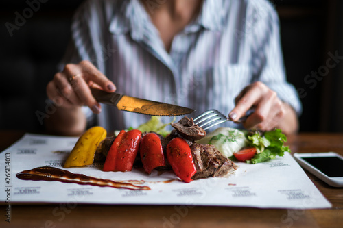 Spicy grilled lamb leg with vegetables and herbs on a roasting cast iron. Barbecue lamb with vegetables. Healthy food. Eating and leisure concept. Woman having dinner at table with food. Toned image.