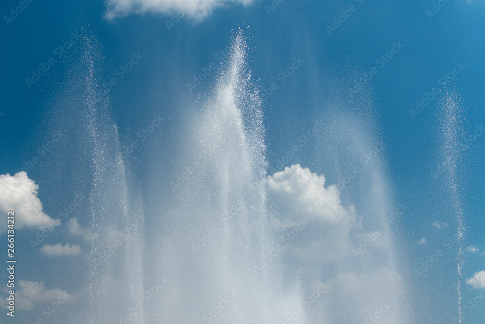 Fountain splashes against the blue sky and white clouds as a background Fountain splashes against the blue sky and white clouds as a background