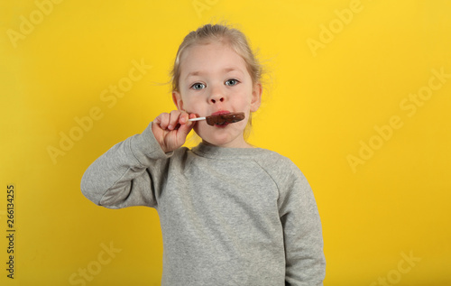 Cute girl child eating sweet chocolate candy on yellow background. Happy childhood.