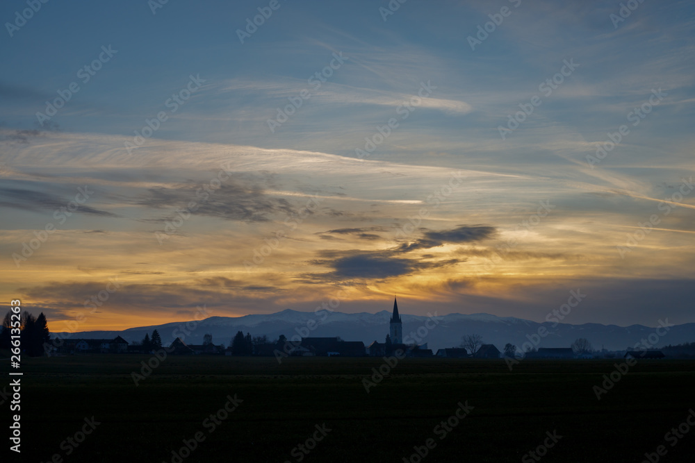 colorful sunset with different types of clouds and a hill and valley silhouette with a church tower in the austrian alps in styri