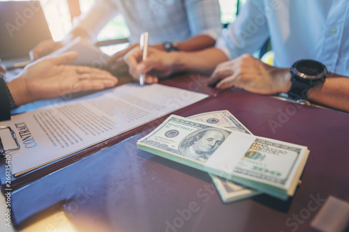 Businessman puts signature on contract at business meeting and passing money after negotiations with business partners
