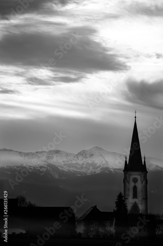 Sunset in a foggy mystic scenery with clouds and a mountain silhouette with a church tower in the austrian alps © woitzel