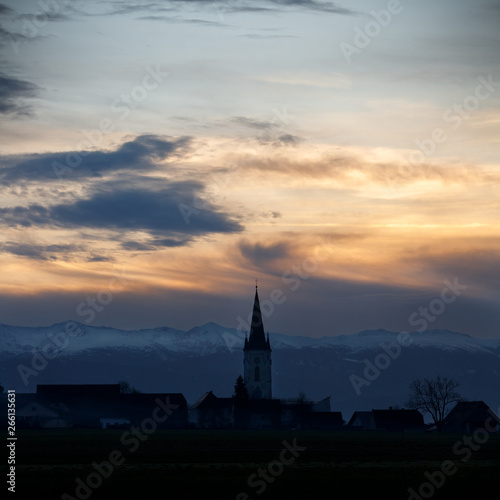 colorful sunset with different types of clouds and a hill and valley silhouette with a church tower in the austrian alps