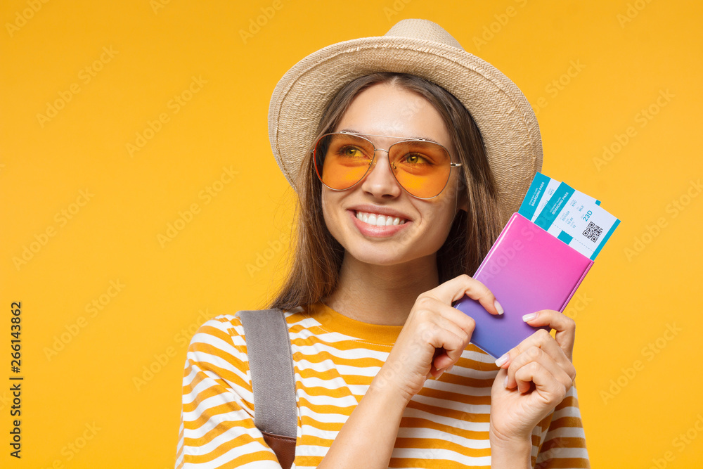 Close-up studio portrait of smiling dreaming young female tourist holding flight tickets, isolated on yellow background Close-up studio portrait of smiling dreaming young female tourist holding flight tickets, isolated on yellow background