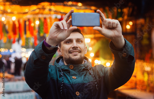 Young man taking photo with phone on the street decorated with colorful flags