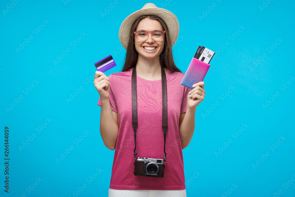 Young female tourist holding credit card and passport with tickets, ready to flight, isolated on blue background Young female tourist holding credit card and passport with tickets, ready to flight, isolated on blue background