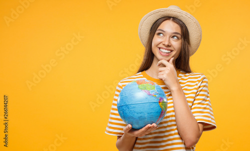 Young female dreaming about future trip, holding globe with one hand, isolated on yellow background. Travel concept.