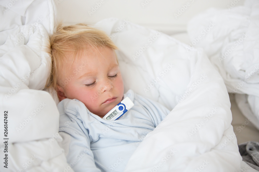 Tired toddler boy with high fever, lying in bed