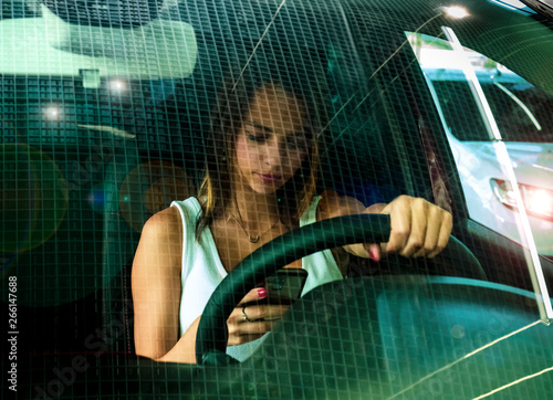 Young woman holding mobile phone while driving car. Female driver hand on steering wheel and checking out her smartphone in moving vehicle. Do not text and drive concept. Close up, background. © kravik93