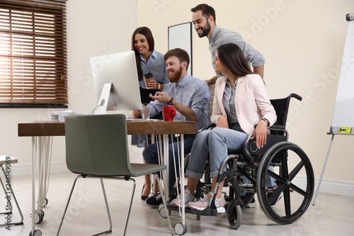 Young woman in wheelchair with colleagues at workplace