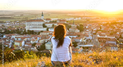 View of sitting young tourist woman overlooking beautiful Mikulov castle from the top of Saint Hill while sunset. South Moravia, wine region in the Czech Republic.