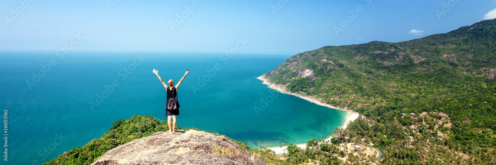 Young woman worth of grief and looks at beautiful bright blue sea, back view. Hands up. Adventure wanderlust lifestyle