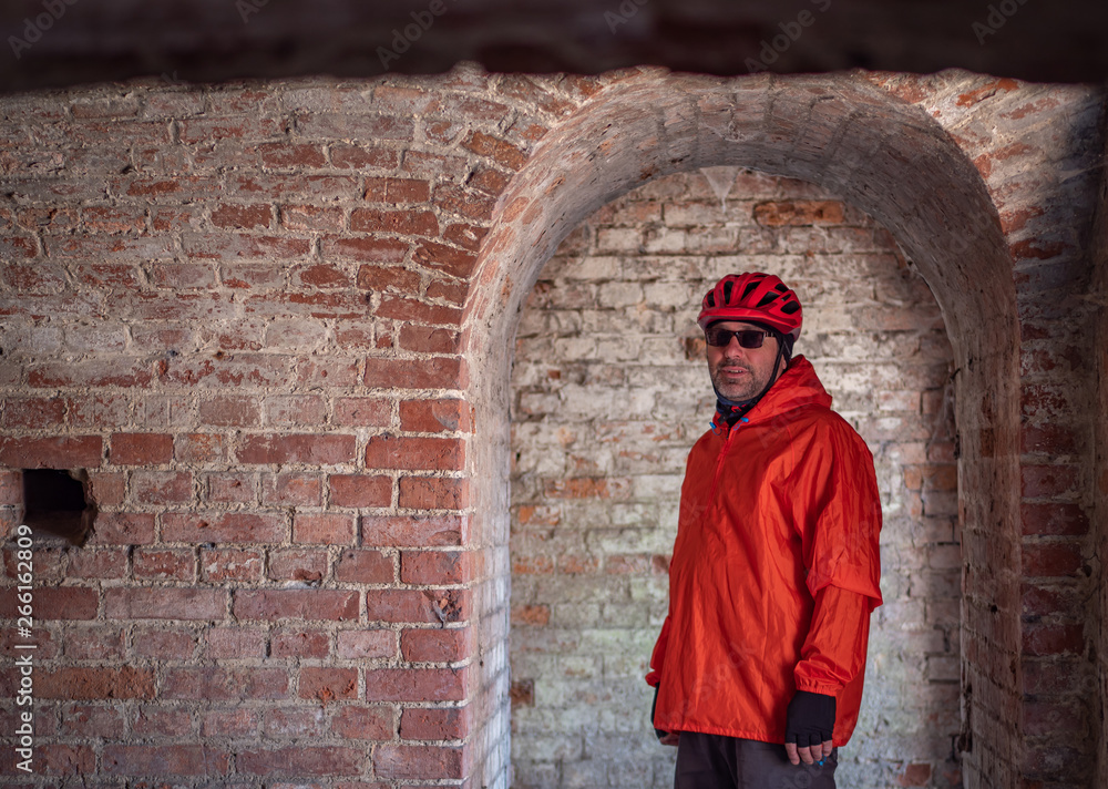 Man wearing bike helmet and orange outfit on his bike trip visiting old 19th century abandoned fortification.