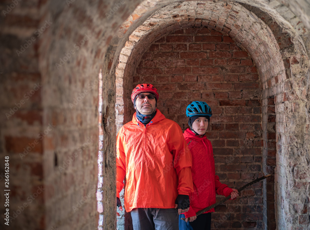 Father and son, wearing bike helmet and orange outfit on his bike trip visiting old 19th century abandoned fortification.