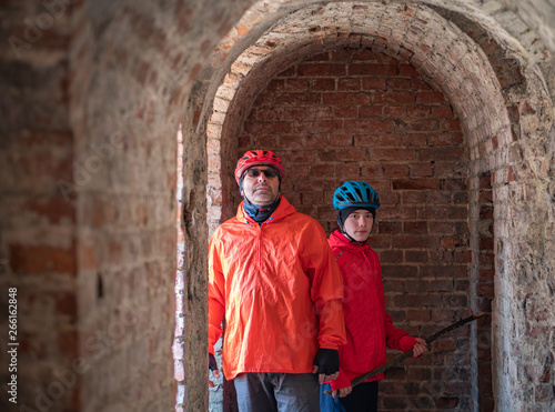 Obraz na płótnie Father and son, wearing bike helmet and orange outfit on his bike trip visiting old 19th century abandoned fortification. w salonie