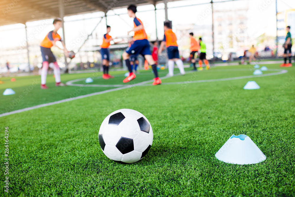 Obraz premium football between marker cones on green artificial turf with blurry soccer team training