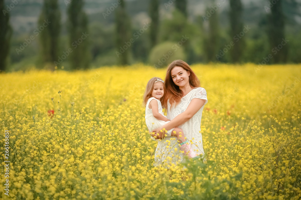 A Happy family: mother with young girl stand hand in hand on a green field against the background of coniferous forest and mountains. A Happy family: mother with young girl stand hand in hand on a green field against the background of coniferous forest and mountains.