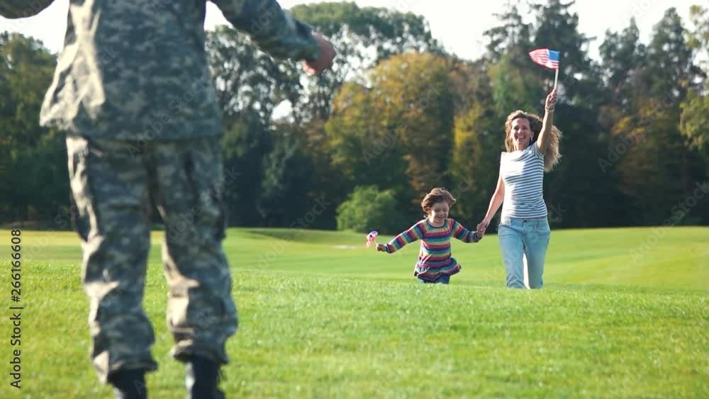 Father came back home from the war. Front view mother and daughter running with usa backgrounds. Meeting at the summer lawn in the park. Father came back home from the war. Front view mother and daughter running with usa backgrounds. Meeting at the summer lawn in the park.