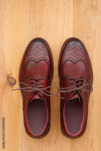 A pair of burgundy men's dress shoes wingtip brogue leather oxford view from above on brown wood background