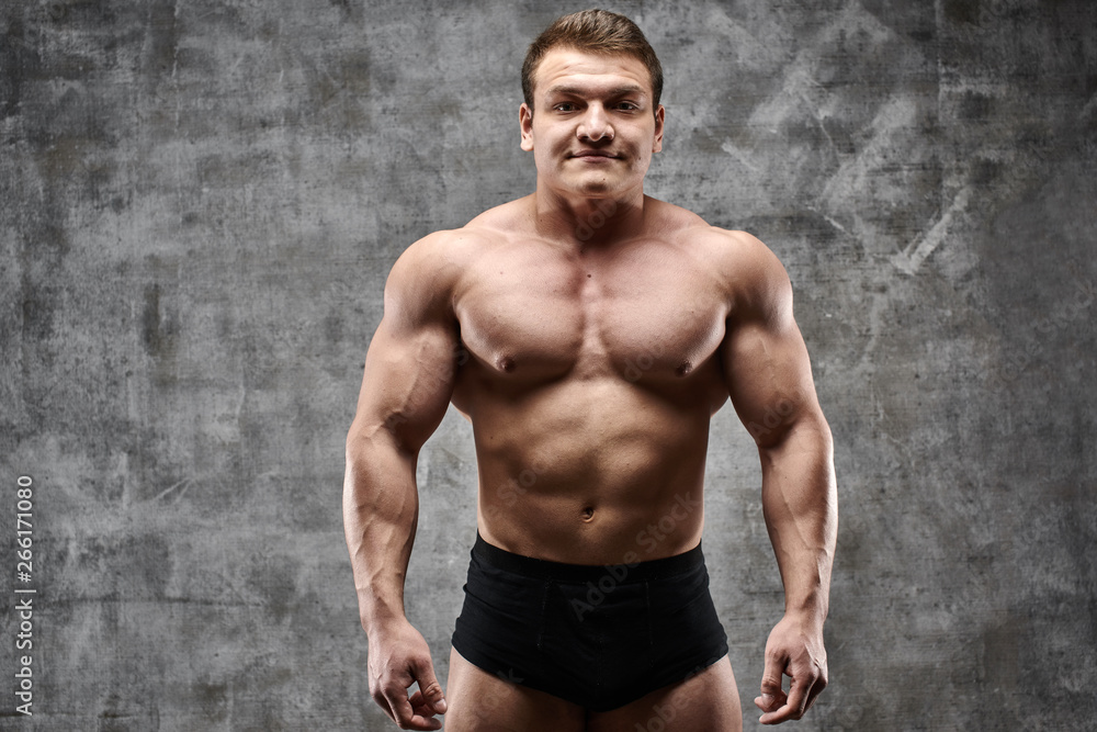 Obraz premium Sexy bodybuilder man posing on dark background in black shorts. Handsome pumped male body isolated with free space for advertising