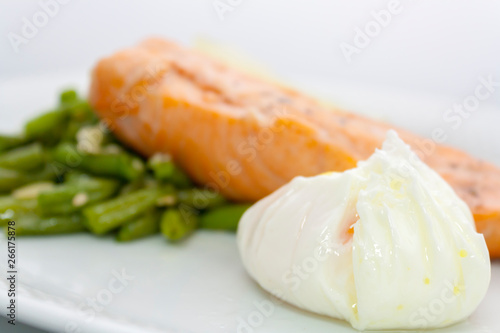 poached egg on the background of salmon steak, beans, sesame and lemon on a white plate