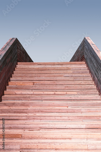 Vertical view of an outdoor wooden stair with a clear sky soft color gradient on the top, reddish tint of wooden steps