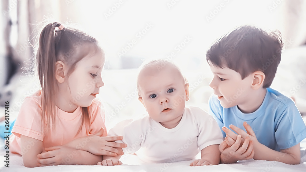 Children lie on the bed next to the newborn baby, little sister. Children lie on the bed next to the newborn baby, little sister.